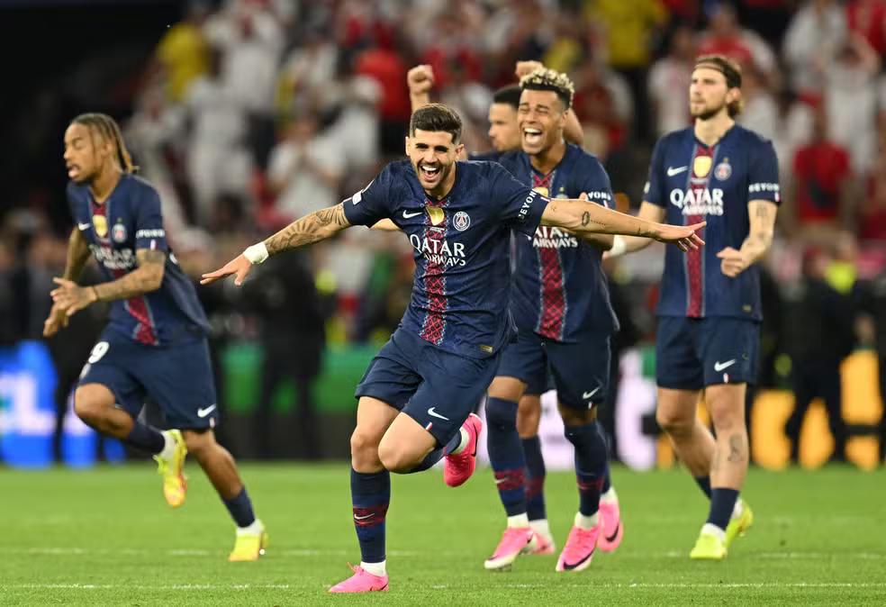 O jogador Lucas Beraldo, do PSG, corre de braços abertos comemorando no gramado, seguido por outros três companheiros de equipe.